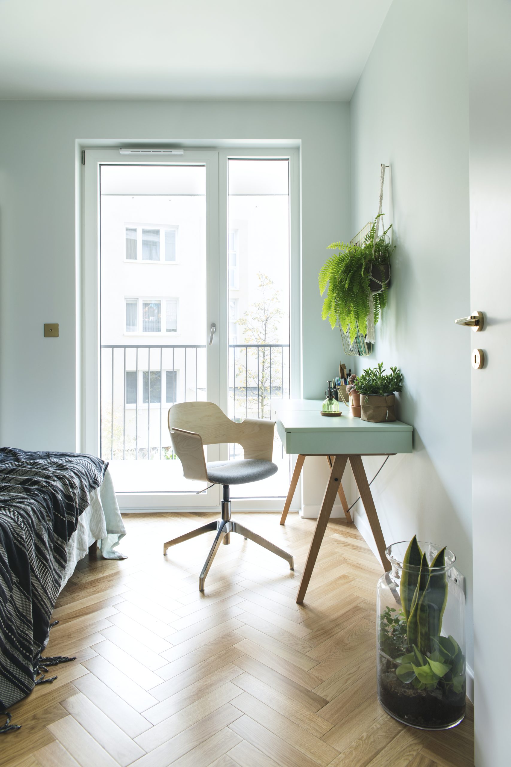 Modern scanidinavian interior of home office with design table, armchair, office accessories, big window and plants. Stylish and sunny space with wooden brown parquet